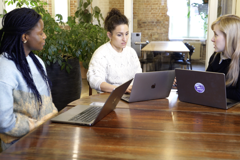 Tre kvinner sitter ved et bord med bærbare datamaskiner.