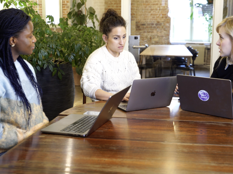 Three women sitting at a table with laptops.