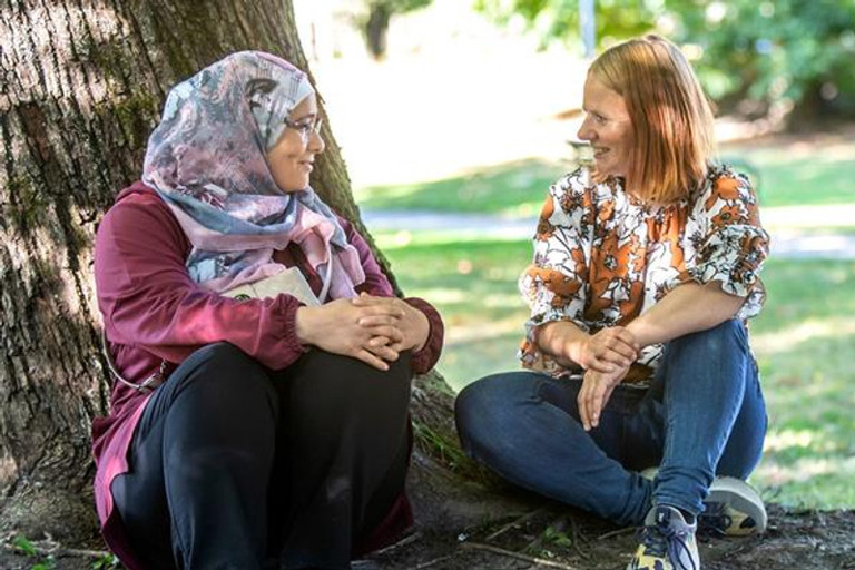 Two women sitting next to a tree talking.