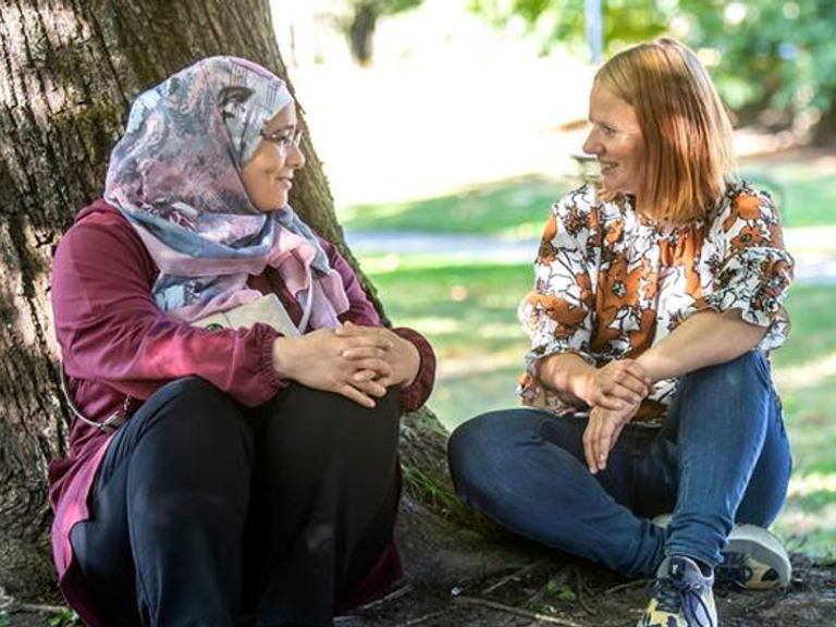 Two women sitting next to a tree talking.