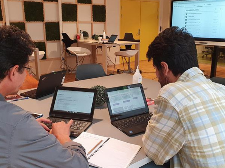 Two men sitting at a table with laptops.