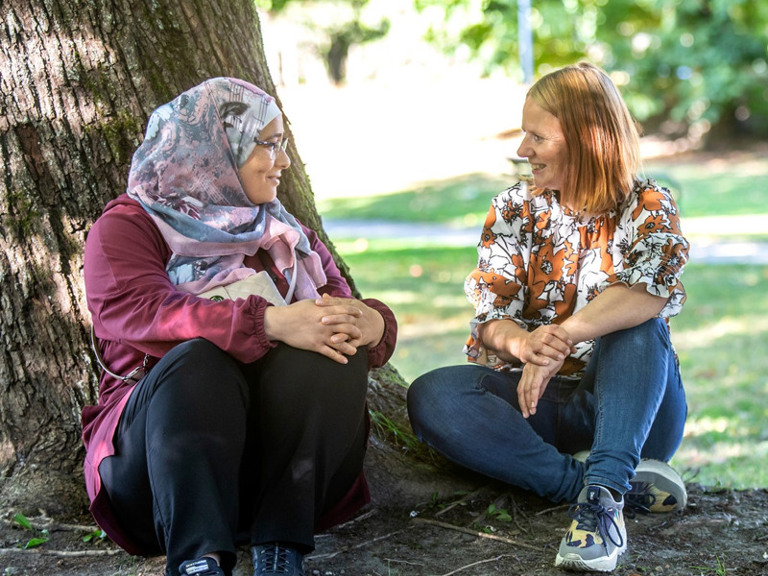 A couple of women sitting next to a tree.