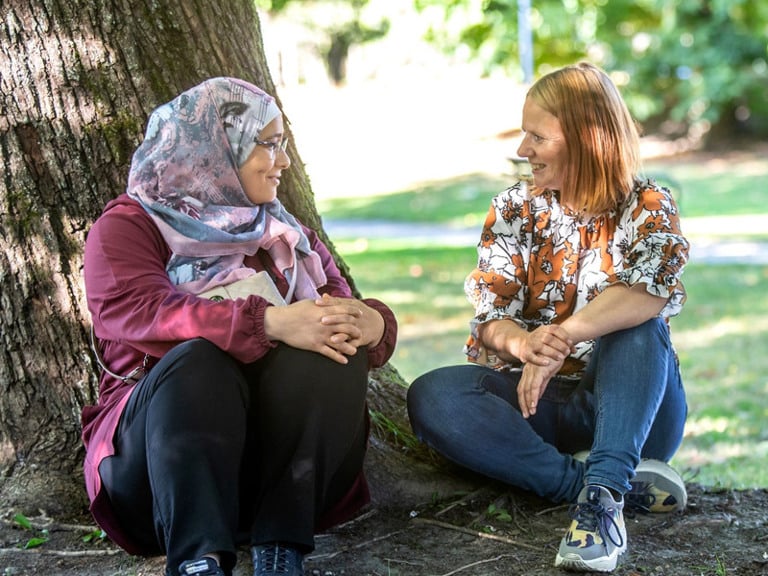 A couple of women sitting next to a tree.
